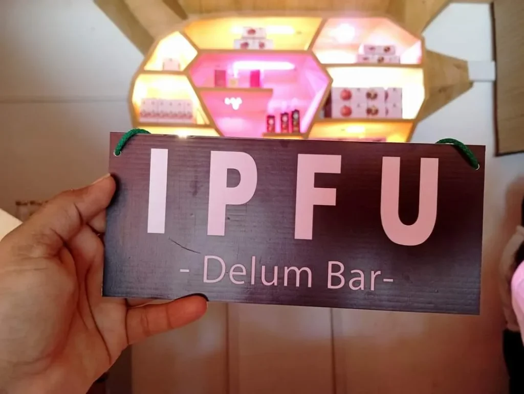 Hand holding an “IPFU – Delum Bar” signboard inside a modern pomegranate product outlet